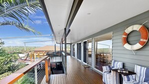 Eine überdachte Holzterrasse mit Sitzgelegenheit und gestreiften Kissen sowie einem Rettungsring an der Wand.