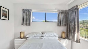 Ein Schlafzimmer mit einem Bett, zwei Nachttischen, einem Vorhangfenster und einem gerahmten Bild an der Wand.