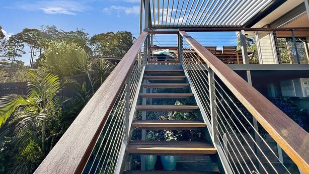 Eine moderne Treppe mit Metallgeländern und Holzstufen, die zu einer Glastür führt.