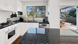 Eine moderne Küche mit weißen Schränken, einer Granit Arbeitsplatte und einem großen Fenster mit Blick auf einen Garten.