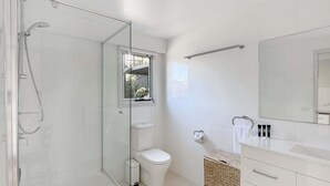 A modern bathroom with a glass shower enclosure, a toilet, a sink with a mirror, and a small window. - Spacious Beach Studio With Alfresco Dining (Surf Beach)