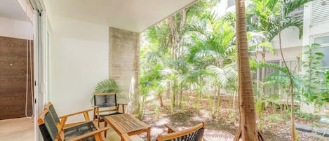 A patio with a table and chairs, surrounded by lush greenery and a tall tree.