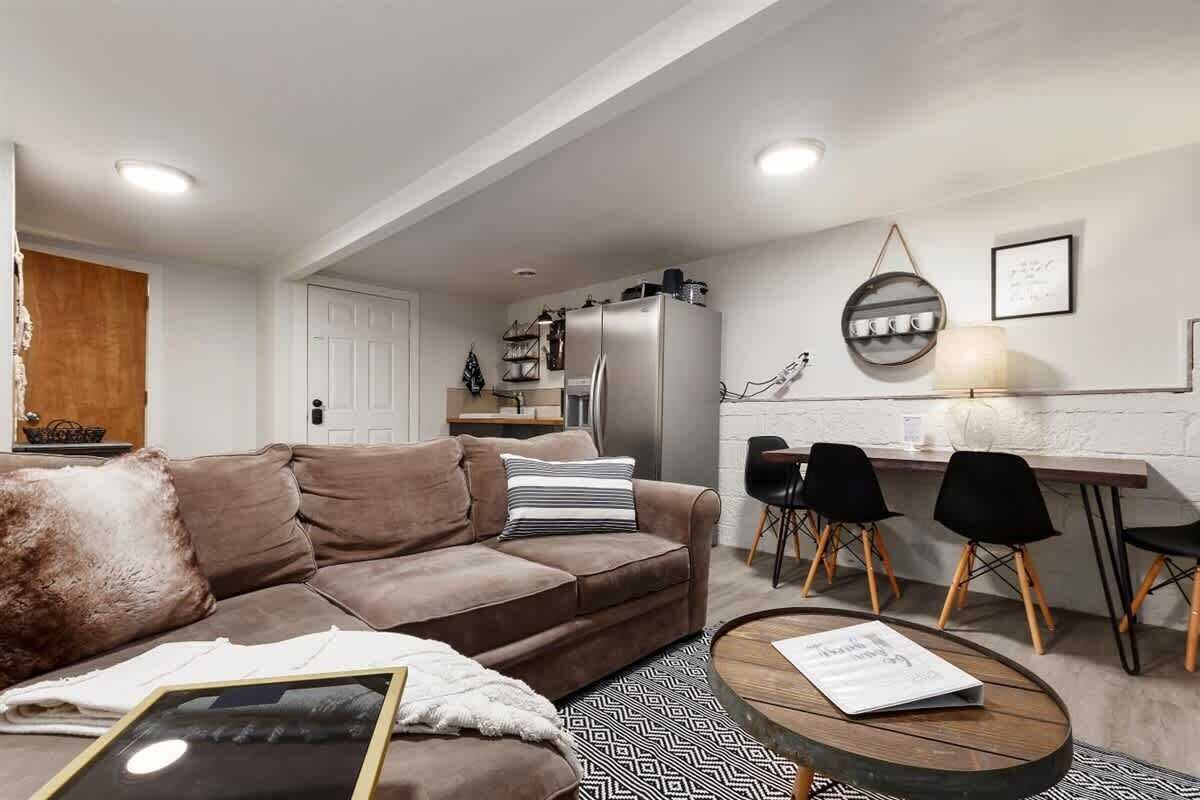 A modern living room with a brown sofa, a glass coffee table, and a dining area with a wooden table and black chairs.