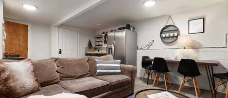 A modern living room with a brown sofa, a glass coffee table, and a dining area with a wooden table and black chairs.