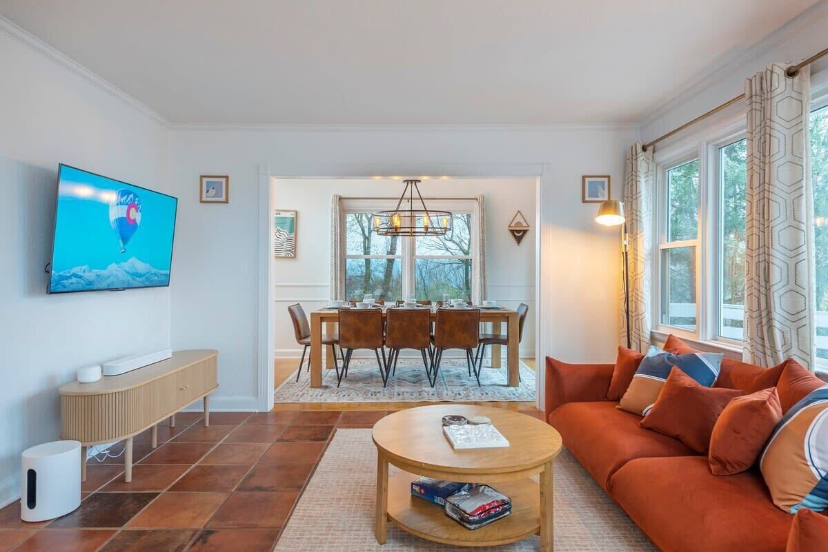 Ein modernes Wohnzimmer mit Fernseher, eine Essecke mit Tisch und Stühlen sowie eine Couch mit Kissen.