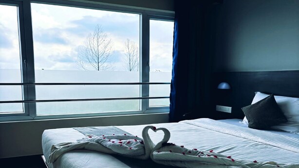 A hotel room with a large window, a bed with a swan-shaped pillow, and a view of the water and trees. - Mist View (Kodaikanal)