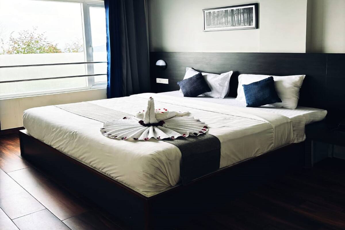 Un cuarto de hotel con una cama grande, vista a árboles por la ventana y un cuadro en la pared.