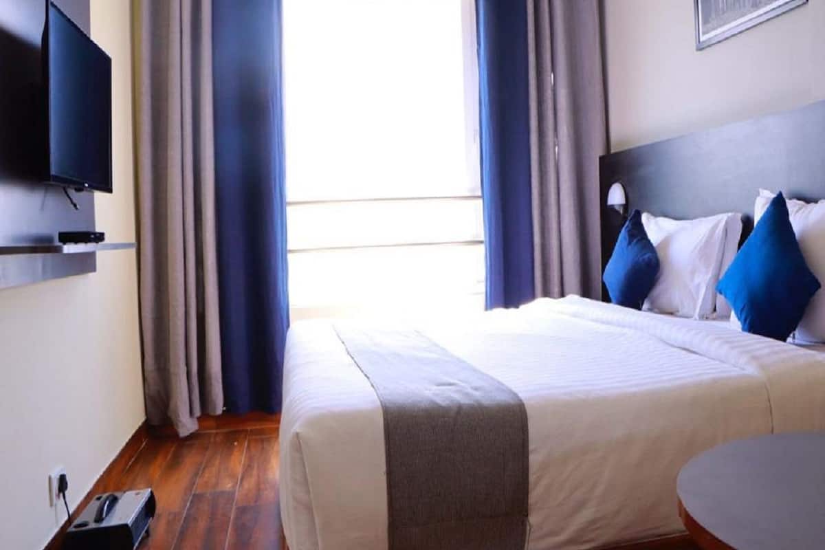 Habitación de hotel con cama, televisor montado en la pared, escritorio y ventana con cortinas.
