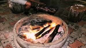 A person cooking outdoors with a fire pit and a grill. - Mist View (Kodaikanal)