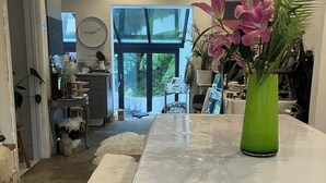 Uma cozinha moderna com bancada branca, um vaso verde com flores e vista para o exterior através de grandes janelas.