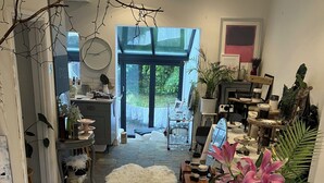Uma sala de estar espaçosa com uma grande janela, um sofá branco, um tapete macio e um vaso verde com flores cor-de-rosa.