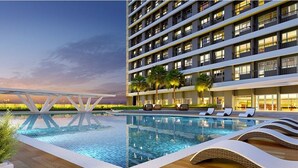 Un hotel moderno con piscina en la azotea, varios balcones e iluminación exterior destacada.