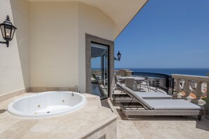 Un balcón con una bañera blanca, sillones de descanso y vista al mar.
