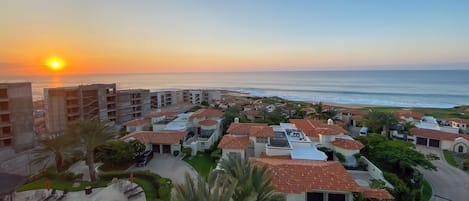 A coastal residential area with a swimming pool, parked cars, and houses with red-tiled roofs.