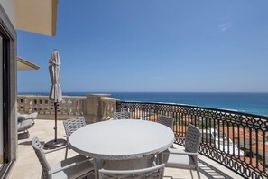 A round table with chairs and a patio umbrella on a balcony overlooking the ocean.