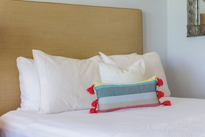 A bed with white bedding and a headboard, a pillow with a geometric pattern, and a decorative pillow with tassels.