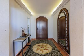 A hallway with a wooden door, a console table with a sculpture, a patterned rug, and a large mirror.
