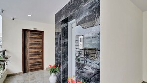 A modern entrance with a marble wall, a wooden door, and a white wall-mounted device. - iROOMZ Ikon Stay (Hyderabad)