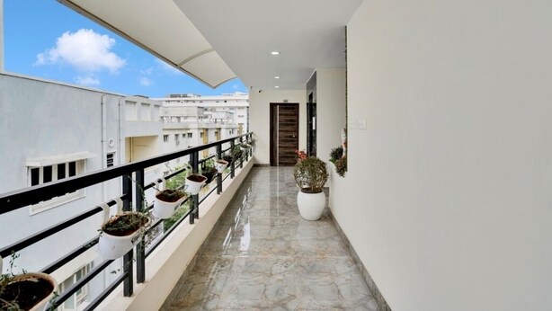 A corridor with potted plants, a marble floor, and a view of buildings in the background. - iROOMZ Ikon Stay (Hyderabad)