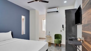A modern hotel room with a bed, a ceiling fan, an air conditioning unit, a television mounted on the wall, and a small green chair. - iROOMZ Ikon Stay (Hyderabad)