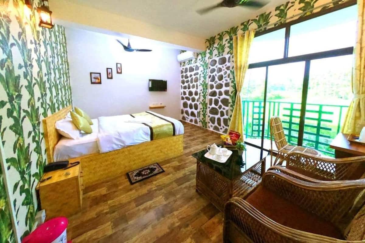 A bedroom with a bed, a desk, wicker furniture, a stone wall, and a balcony with a view.