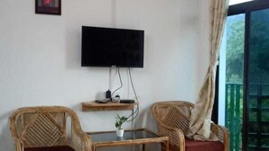 Ein Schlafzimmer mit einem Bett, zwei Korbstühlen, einem kleinen Tisch, einem Fernseher und einem Fenster mit Vorhängen.