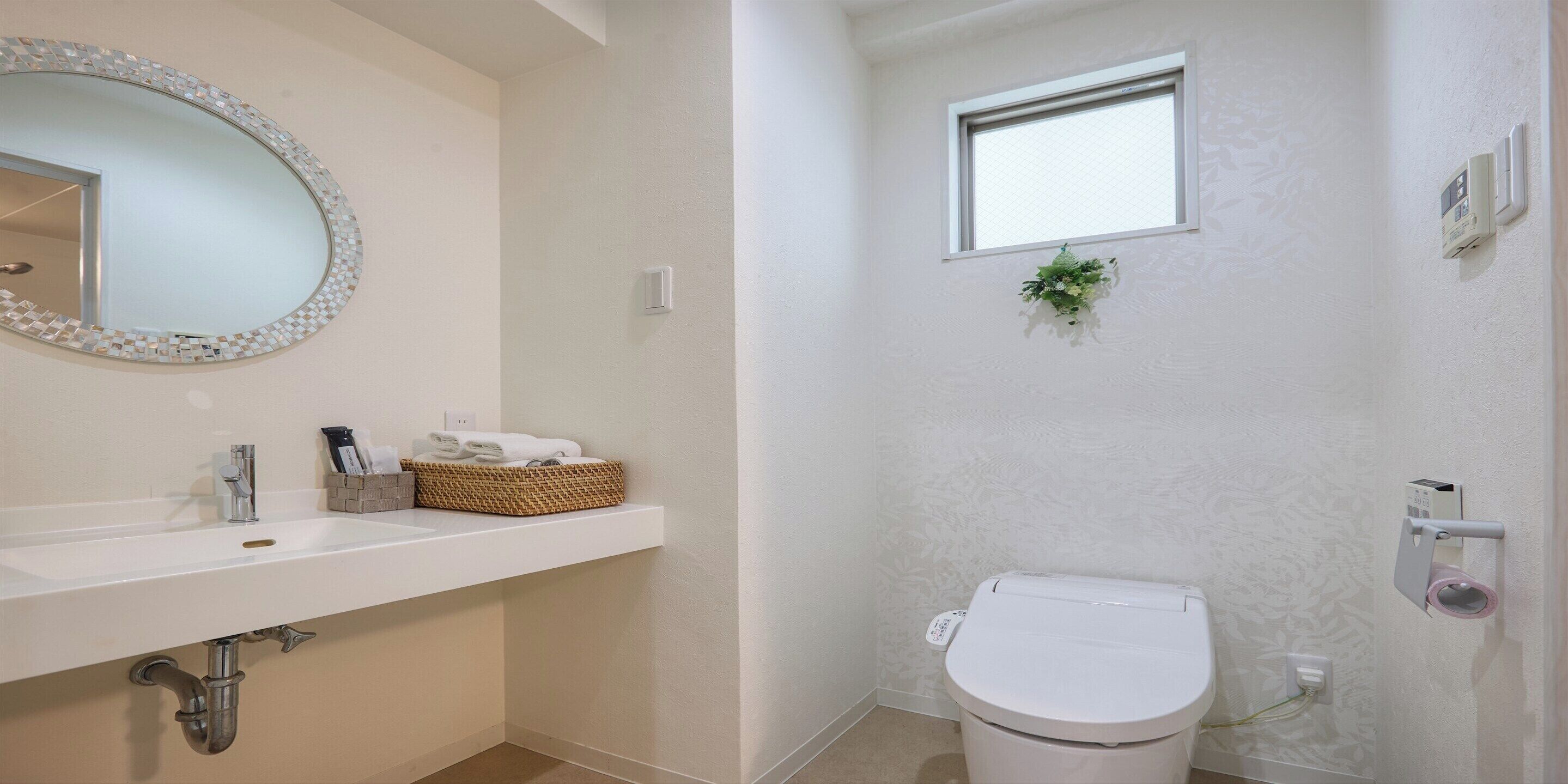 A bathroom with a white sink, a round mirror, a toilet, and a small window.