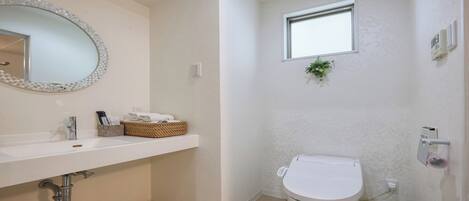 A bathroom with a white sink, a round mirror, a toilet, and a small window.