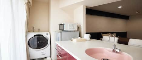 A hotel room with a washing machine, a microwave, a sink, and a bed with a headboard.