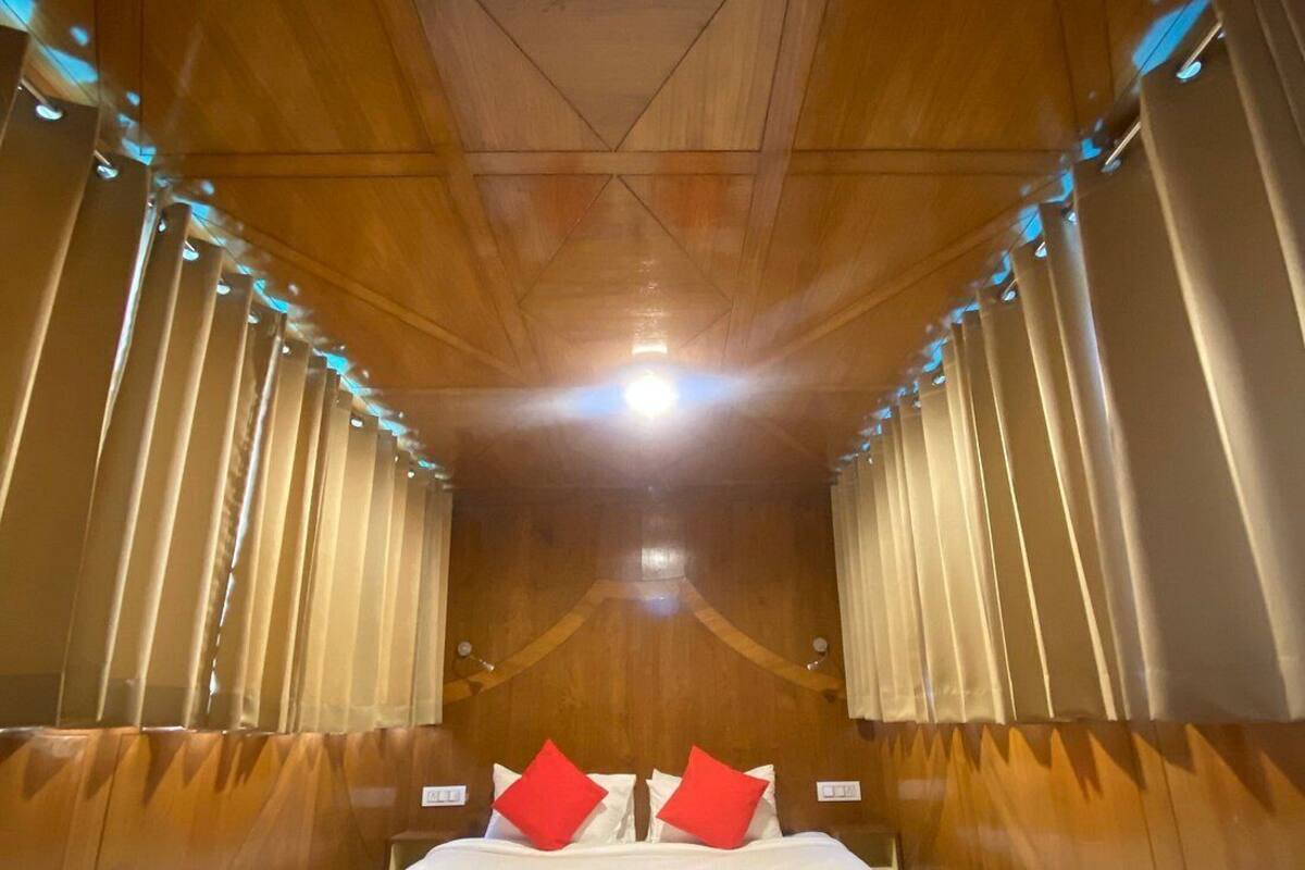 Ein schmales Zimmer mit Holzvertäfelung, ein Bett steht in der Mitte zwischen zwei Vorhängen.