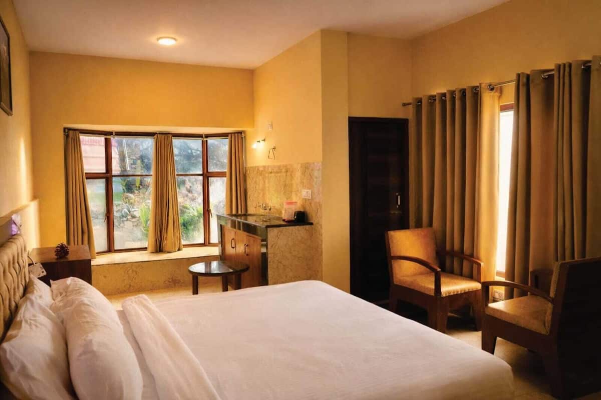 Ein Hotelzimmer mit Bett, Schreibtisch, Stuhl, einem Fenster mit Vorhängen und Blick auf Grünflächen.