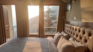 A bedroom with a large bed, a wooden headboard, and a view of trees through the windows. - The Jungle Story By Headquarter (Shimla)