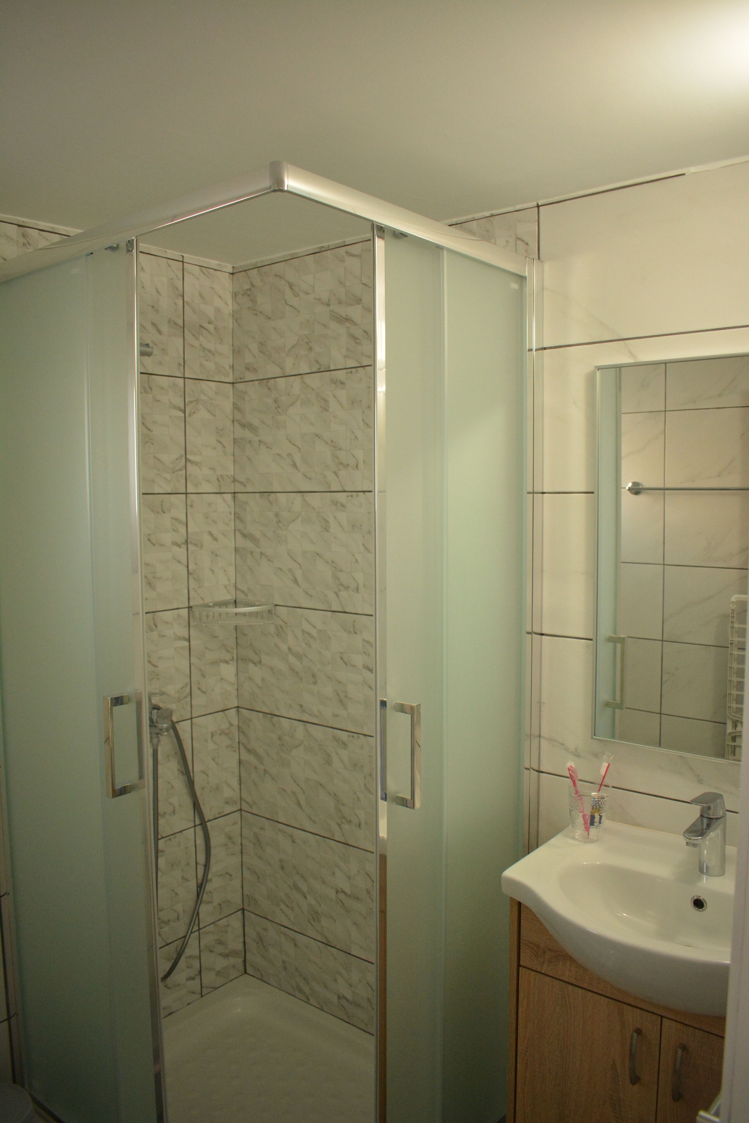 Un baño con ducha envuelta en vidrio, un lavamanos con espejo y un armario de madera.