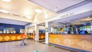 Ein Hotel-Empfangsbereich mit einem 'Check-In'-Schalter, einem Concierge-Schalter und einem gefliesten Boden mit Wegweisern.