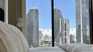 Une chambre dotée d’une grande fenêtre donnant sur des immeubles imposants et un ciel dégagé.