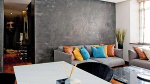 A modern living room with a grey sofa adorned with colorful cushions, a white coffee table, and a large grey textured wall. - Luxury Knightsbridge Apartment near Harrods (Greater London)