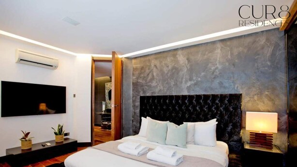 A modern bedroom with a large bed, a flat-screen TV, a bedside table with a lamp, and a built-in air conditioner. - Luxury Knightsbridge Apartment near Harrods (Greater London)