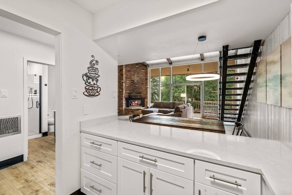 A modern kitchen with a large island, a fireplace, and a view to a living area.