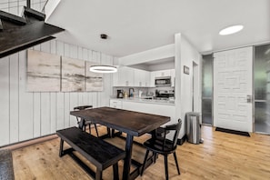 A modern kitchen with white cabinets, a wooden dining table, and a bench.