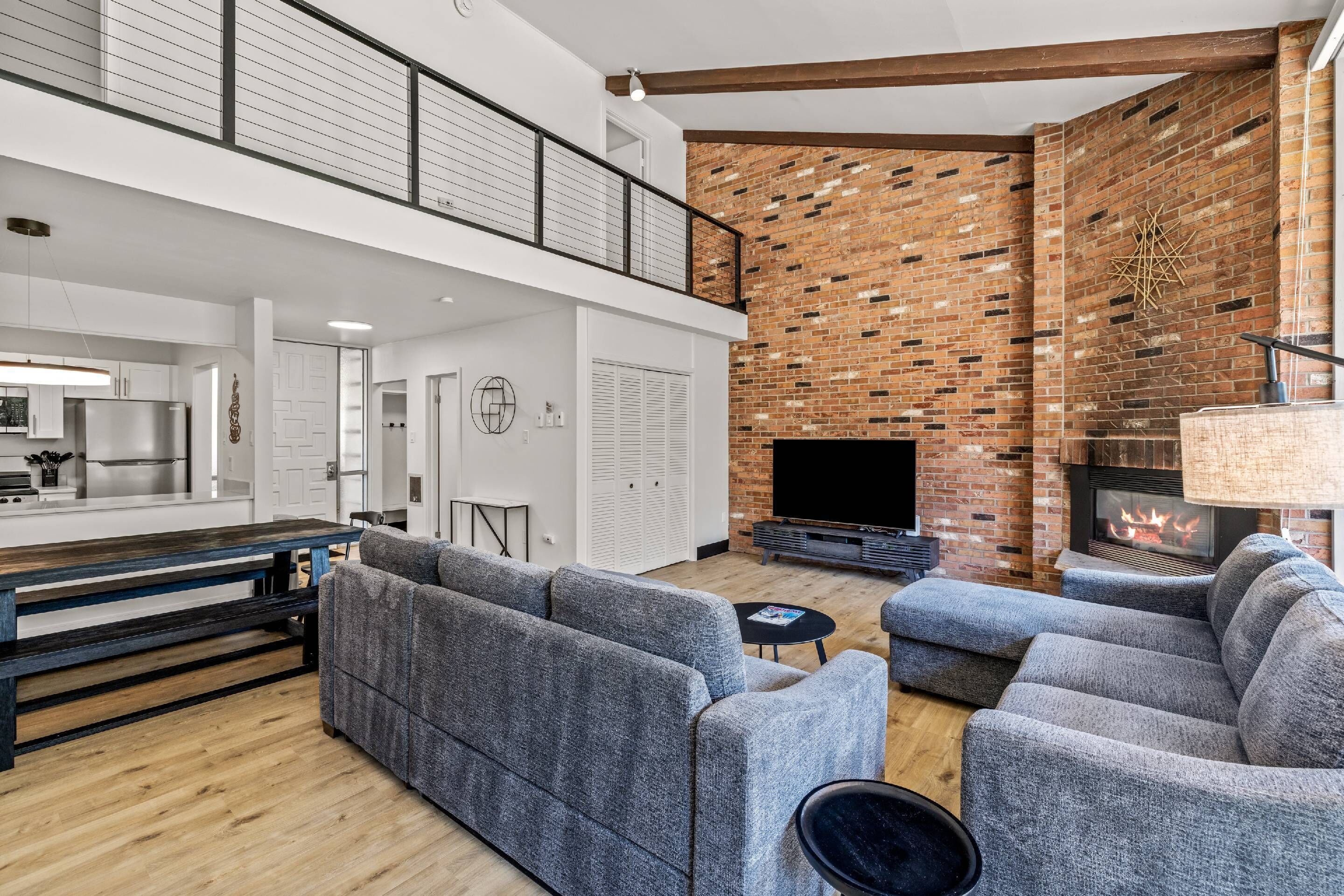 Una sala moderna con chimenea, sofás grises y una cocina al fondo.