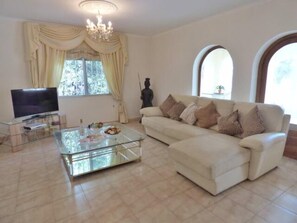 Relax in this stylish living room with a large flat-screen TV, comfortable sofa, and chandelier.