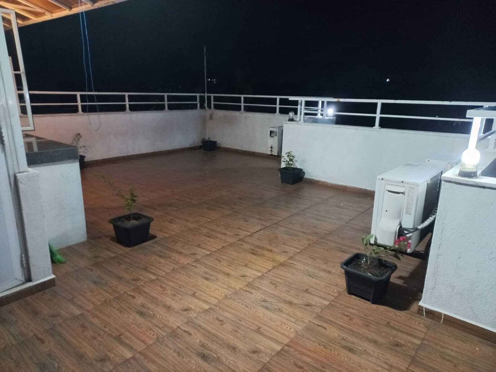 A rooftop terrace with wooden flooring, potted plants, and a white railing.