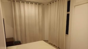 Een slaapkamer met een bed, gordijnen, een raam en een klein tafeltje.