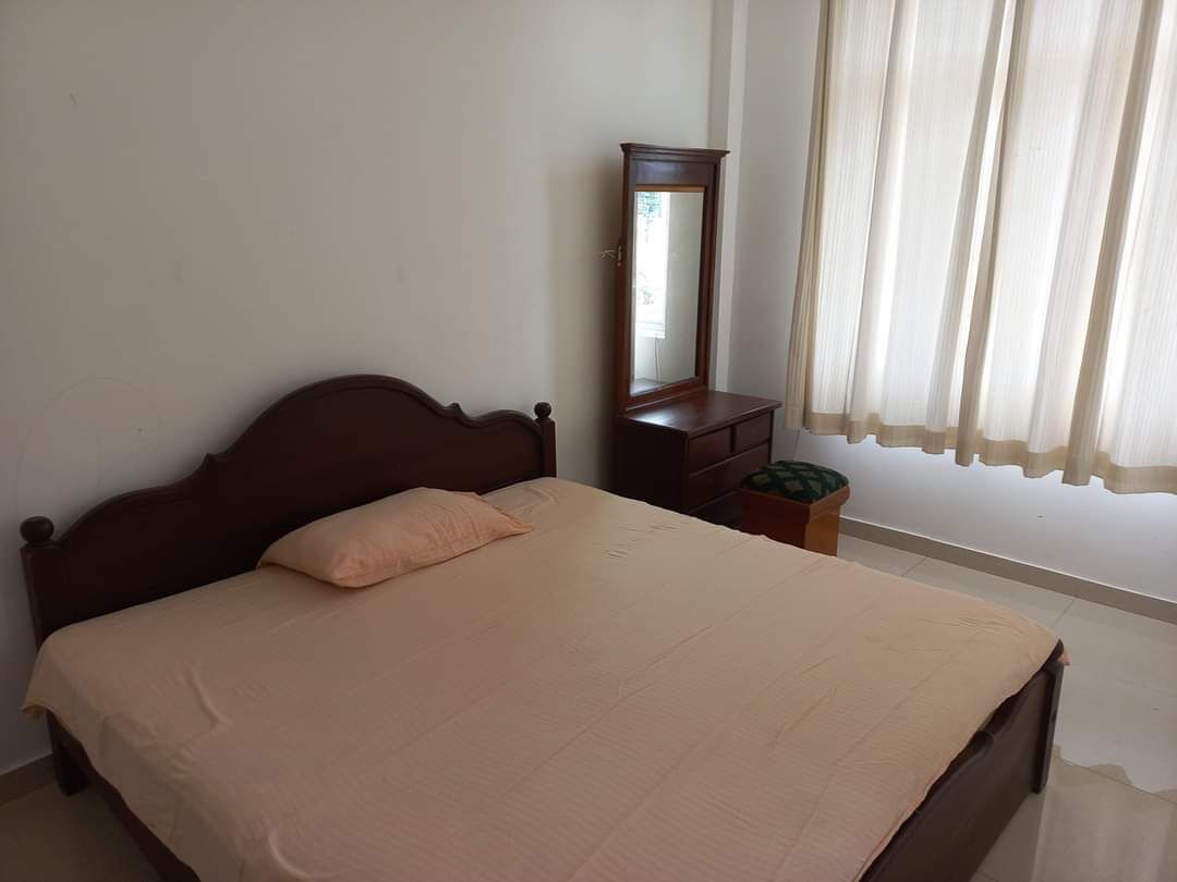 A bedroom with a single bed, a dresser, a mirror, and a window with curtains.