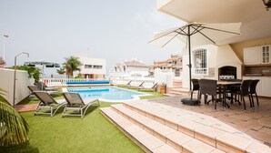 A swimming pool with lounge chairs, a patio with a table and chairs, and a view of neighboring buildings.