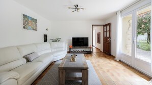 A living room with a sofa, a coffee table, a TV, and a door leading to a balcony. - Maison de Campagne- mas Célestin Avec Piscine 6 Personnes - 3 Chambres (Camaret-sur-Aigues)