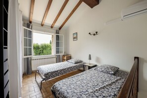 Un dormitorio con dos camas, una ventana con vistas, un radiador y una lámpara fijada a la pared.