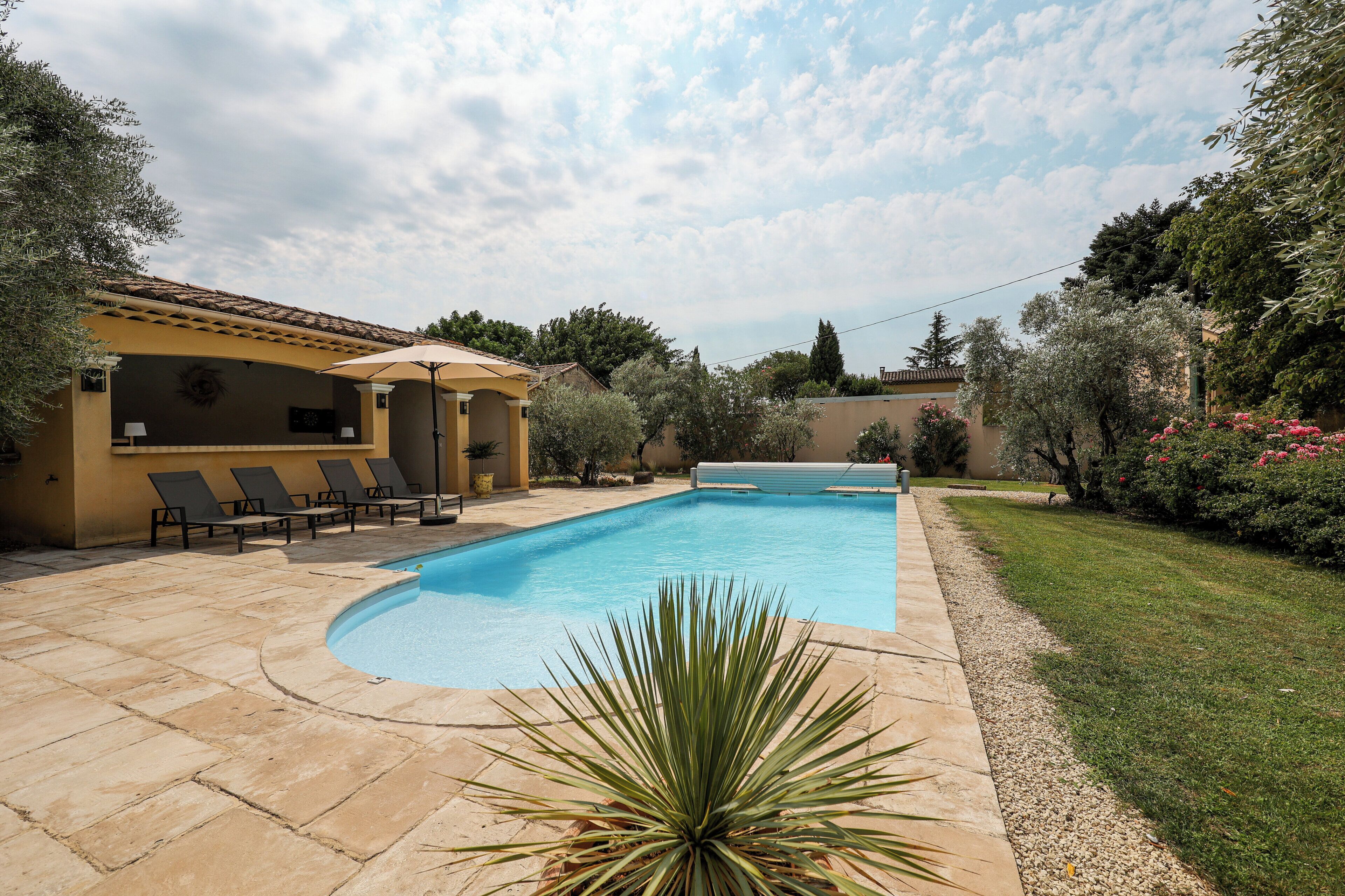 Une piscine à bords incurvés, entourée d’une terrasse agrémentée de chaises longues et d’un petit jardin.