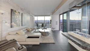 Una sala de estar moderna con un sofá, una mesa de centro y vistas de la ciudad a través de amplios ventanales.