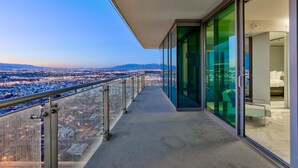 Un balcón con baranda de vidrio que da a una vista panorámica de la ciudad al atardecer.